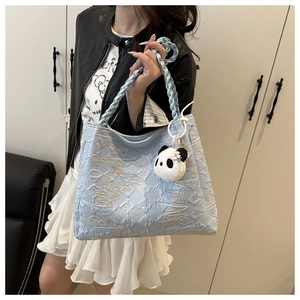 Close-up of light blue quilted tote bag with embroidery and panda plush pendant accessory