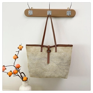 Detail of hand-woven beige straw tote bag with brown leather handles on wooden hook