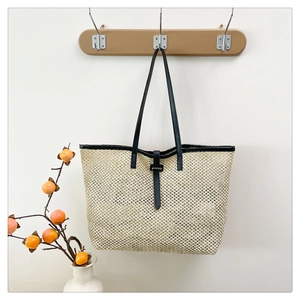 Macro shot of large straw tote with black leather straps hanging on a wooden wall hook