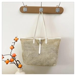 Detail of summer straw tote bag with white leather straps hanging on a wooden hook