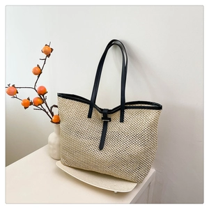 Detail of woven straw tote bag featuring contrast black leather handles and textures