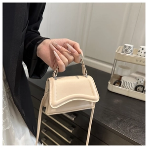 Detailed macro view of the curved base and matte cream leather of the mini handbag