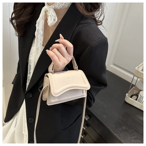 Detail of minimalist beige small square bag with wavy flap design and slim shoulder strap