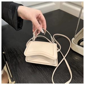 Close-up of beige crossbody bag featuring wave-shaped flap and slender shoulder strap