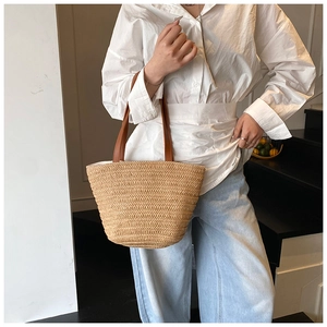 Close-up of handwoven straw tote with premium brown leather handles worn by a model