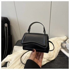 Detail view of mini black leather handbag showing wavy flap design and compact size