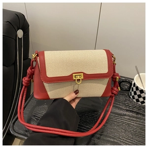 Close-up of red leather and beige canvas baguette bag with golden twist lock on table