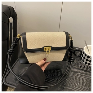 Detail of two-tone shoulder bag featuring beige fabric, black leather, and gold metal lock
