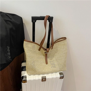 Beige woven tote bag with brown leather straps hanging on a white suitcase