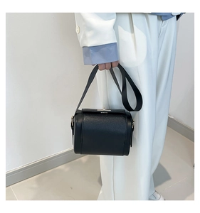 Detail of black lychee grain leather handbag with silver clasp and wide fabric strap