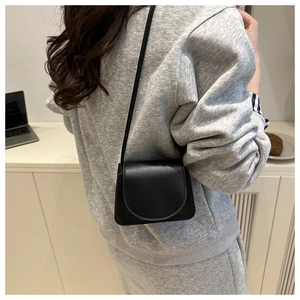 Detailed side view of a black mini crossbody bag with litchi texture on a model