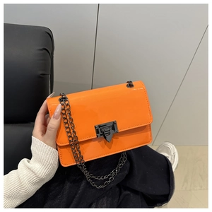 Detail view of orange patent leather crossbody bag with geometric metal clasp and chain strap