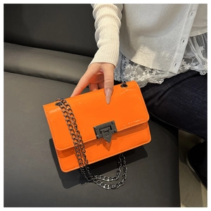 Close-up of bright orange patent leather crossbody bag with gunmetal chain and turn-lock