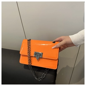 Detail of bright orange patent leather crossbody bag with chain and metallic arrow lock