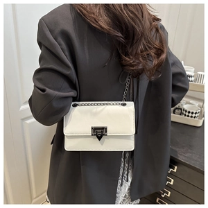 Detail of white leather crossbody bag with a distinctive black metal clasp and chain strap