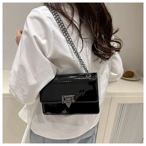 Detail of black patent leather crossbody bag with chain strap and geometric turn-lock clasp