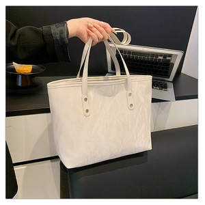 Close-up of white tote bag featuring pleated texture and gold rivet details on handle