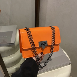 Glossy orange patent leather crossbody bag with metal buckle and chain strap shown held