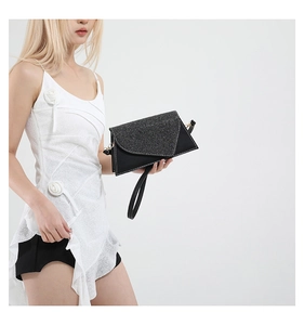 Détail du rabat triangulaire pailleté noir et de la lanière en cuir mat de cette pochette