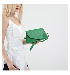 Sac enveloppe vert avec rabat pailleté tenu par un mannequin en robe blanche