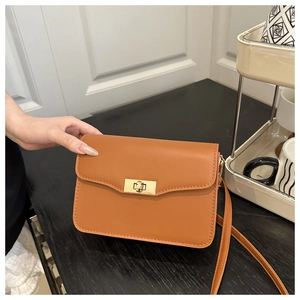 Detailed view of brown leather crossbody bag with golden metal rotary lock and flap closure
