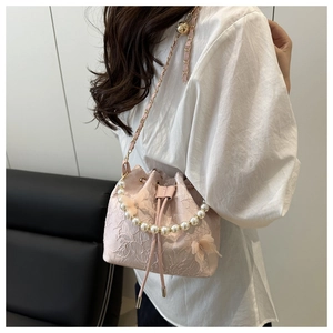Pink lace bucket bag with pearl handle and chain strap worn on shoulder by model