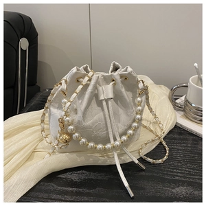 Detailed close-up of white lace bucket bag featuring pearl handle and gold chain strap