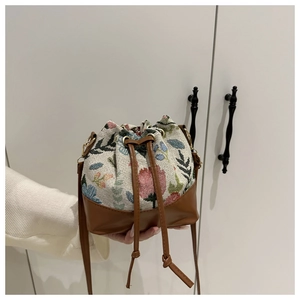 Close-up of floral jacquard bucket bag with brown leather base and drawstring closure