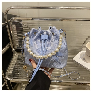 Detail of light blue bucket bag with lace embroidery, butterfly charm and pearl handle