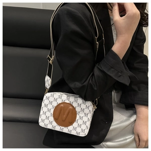 Detail of crossbody camera bag with all-over M-letter pattern and brown leather patch