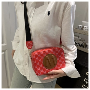 Detail of red monogram camera bag with wide woven strap and 3D M-letter logo patch