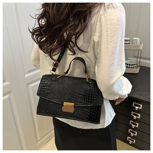 Side view of black faux crocodile pattern handbag with gold clasp on a female model