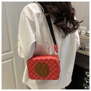 Close-up of red camera bag with monogram pattern and striped wide shoulder strap worn by model