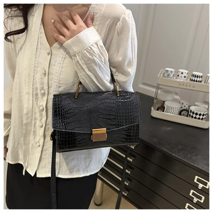Mannequin portant un sac à main noir motif crocodile avec des boucles dorées chic