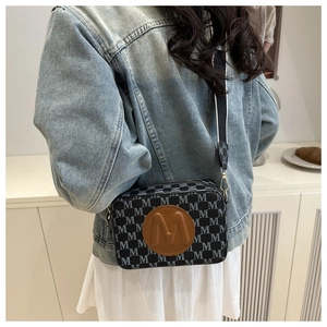Detail of grey monogram crossbody bag featuring brown leather logo patch and wide strap