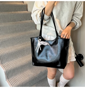 Detail of black glossy tote bag featuring white lace bow and elegant pearl charm