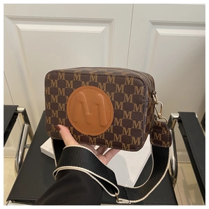 Close-up of vintage brown camera bag with monogram pattern and wide woven shoulder strap