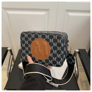 Detail view of monogram camera bag with large brown leather M patch and fabric strap