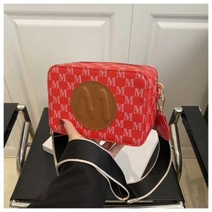 Detail of red crossbody camera bag with all-over M pattern and wide bicolor strap