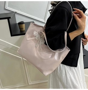 Close-up of pink glossy shoulder bag with pearl lace bow charm and smooth leather finish