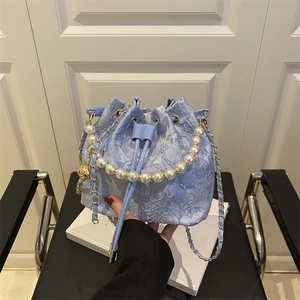 Light blue lace bucket bag with pearl handle and metal chain in an elegant setting