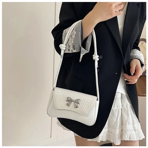 Detail showing white woven texture flap with silver metal bow on a stylish shoulder bag