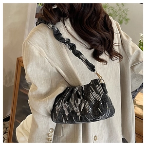 Detail of black pleated cloud bag with silver sequin lines worn by model in beige blazer