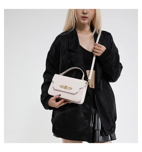 Detail of white leather crossbody bag with gold hardware held by a model