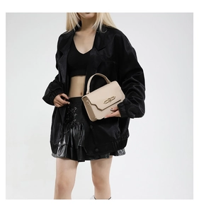 Detail of a creamy off-white leather handbag with gold twist lock on a black outfit