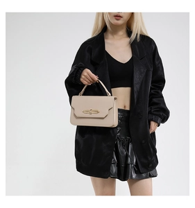 Chic beige leather handbag with gold metal clasp held by model in black outfit
