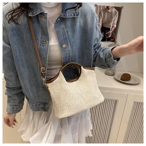 Detail of woven straw tote bag with brown leather handles worn by a model
