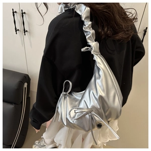Detail of silver metallic shoulder bag showing ruched strap and bow in Y2K style