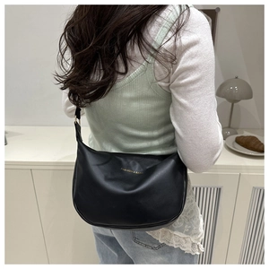 Close-up of black leather shoulder bag with gold logo on model in minimalist interior