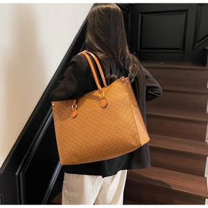 Detail of a brown tote bag with M-pattern print and leather handles in a modern setting